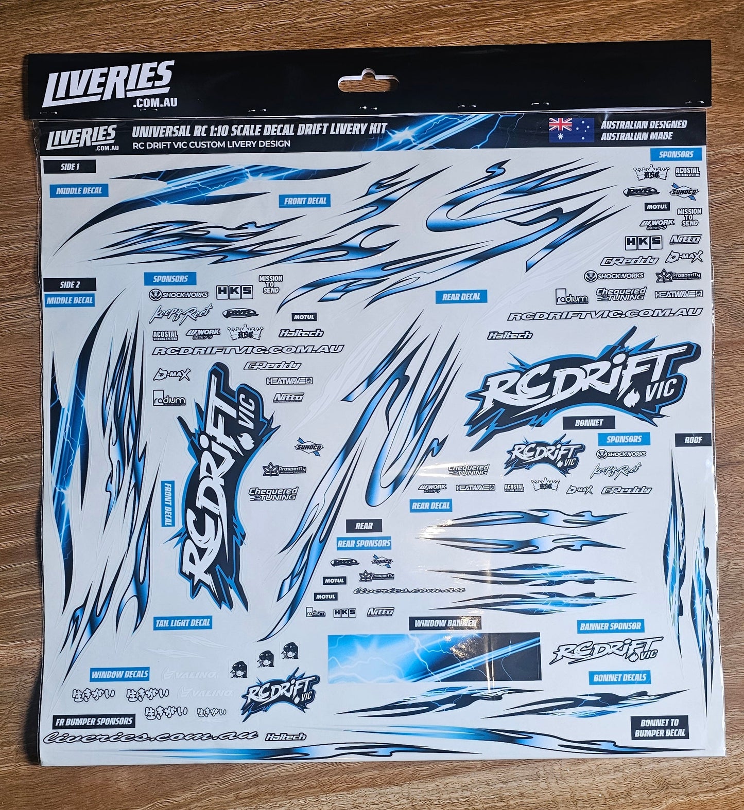RC Drift VIC livery sticker kit – 1:10 scale RC drift decal sheet photographed on wood surface, includes blue lightning designs and RC Drift VIC sponsor logos.